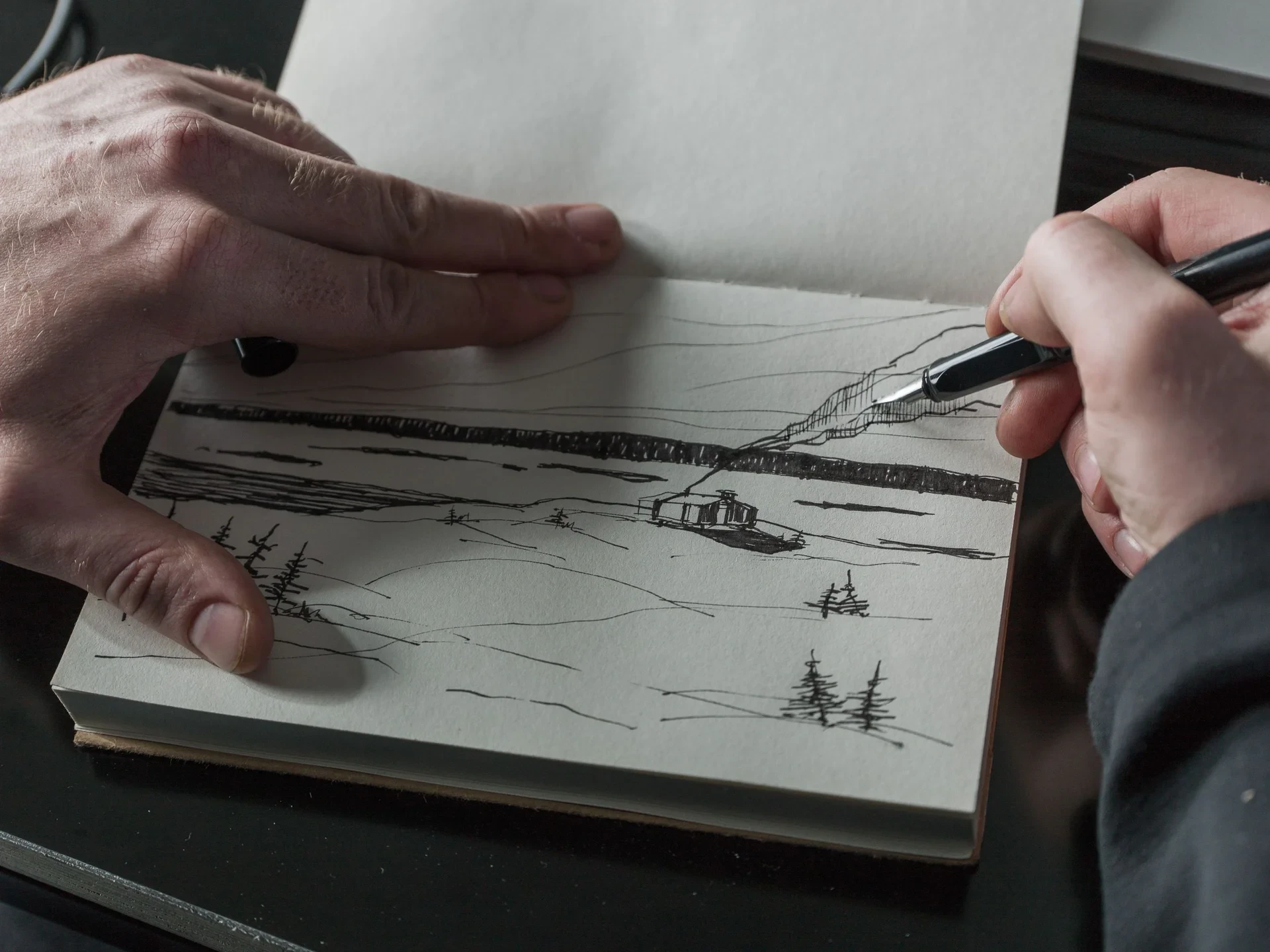 Hands sketching the cabin in a notebook