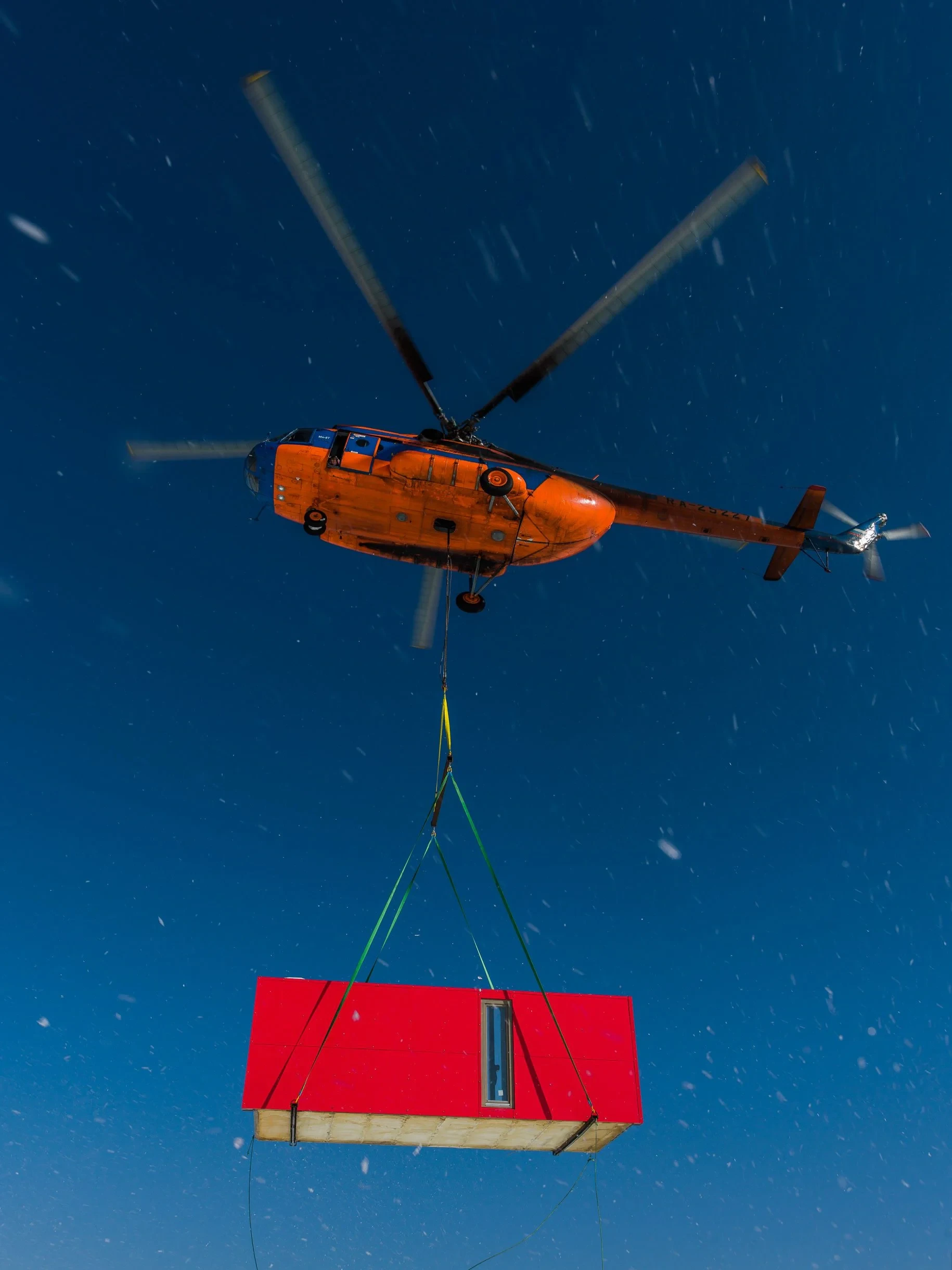 Helicopter lifting red module against blue sky