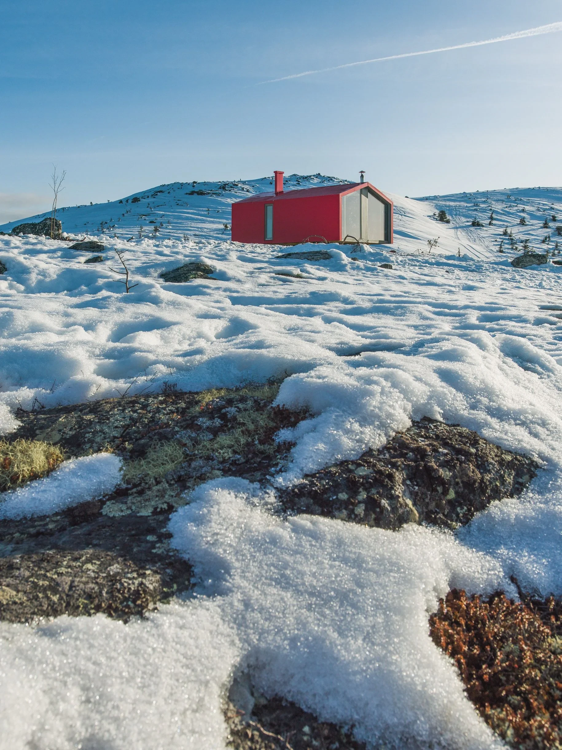 Red cabin on melting snowy hillside
