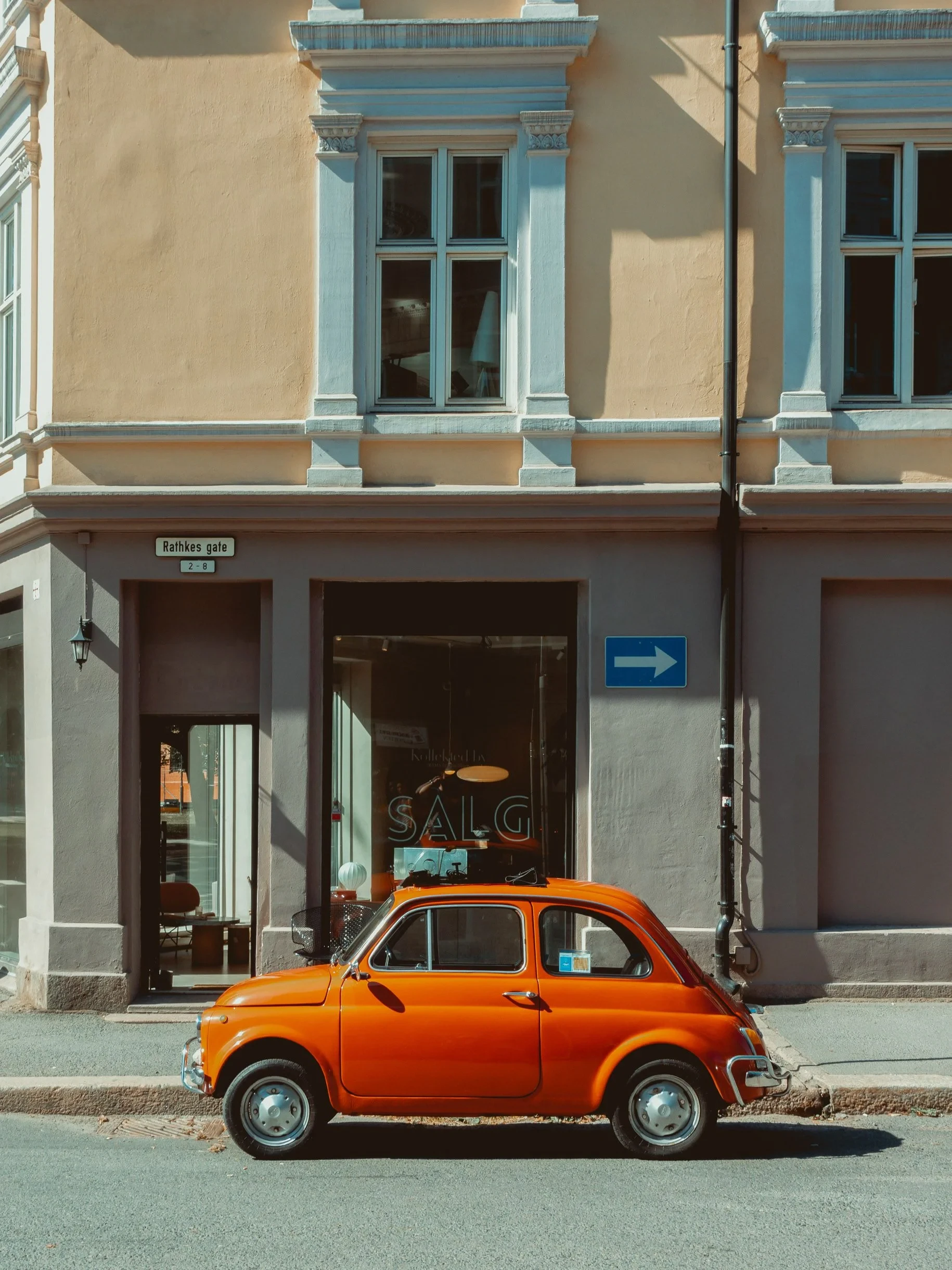 Orange vintage Fiat parked by a shopfront
