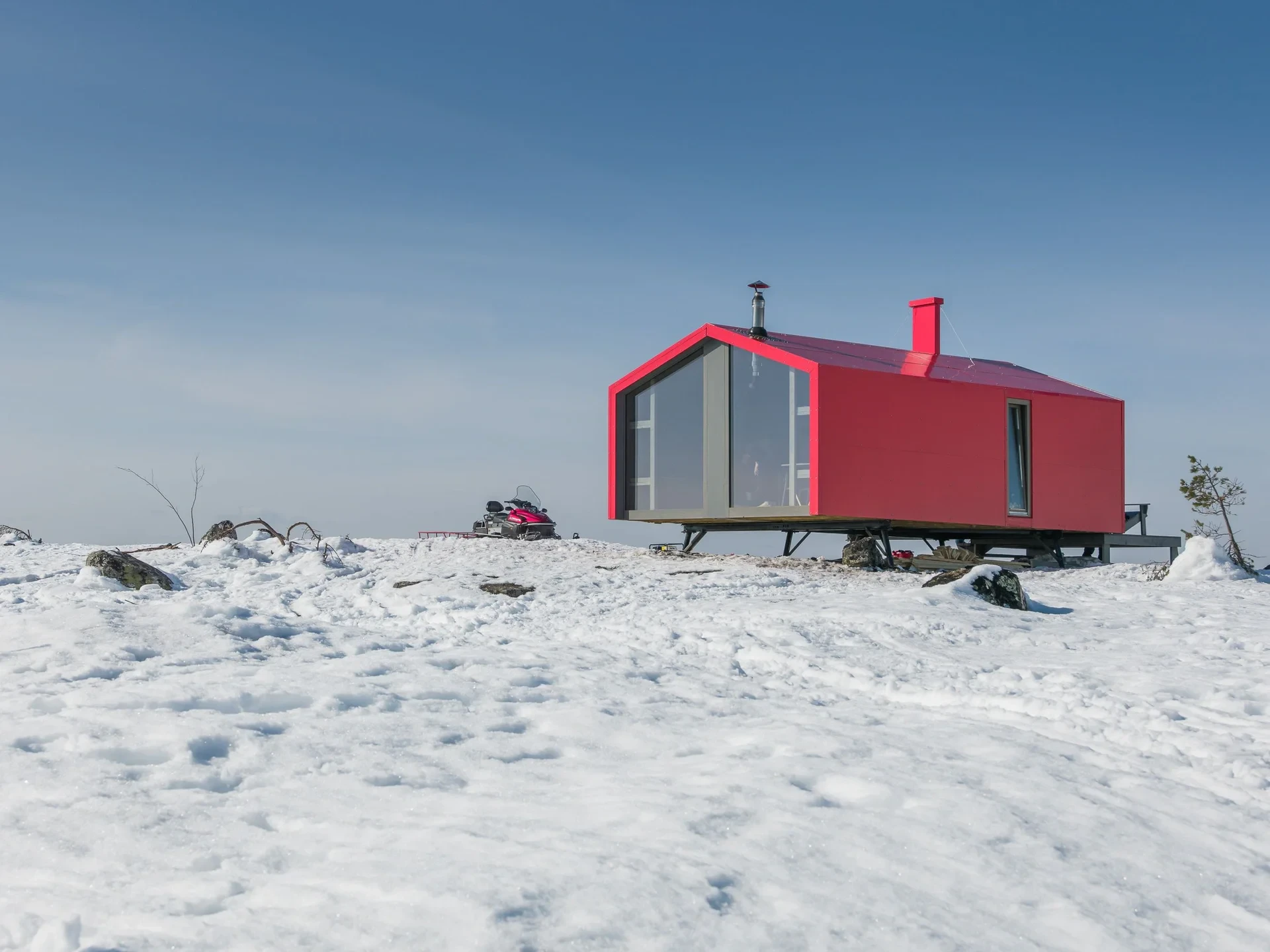 Red modular cabin with snowmobile in snow