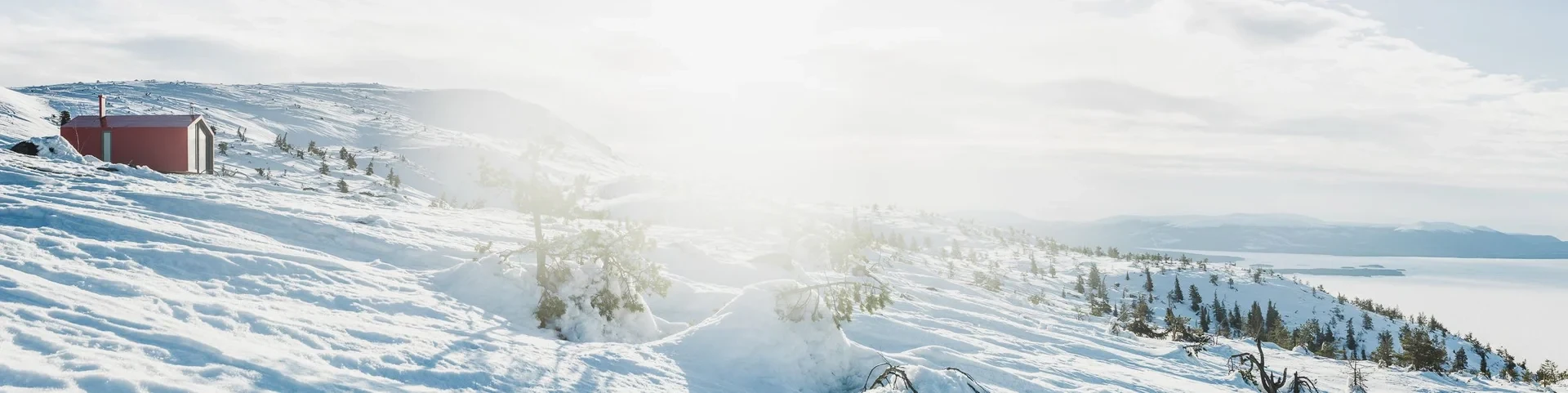 Cabin on sunlit snowy slope above fjord